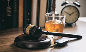 A desk with a gavel, car keys, and a glass filled with alcohol, indicating a DUI case