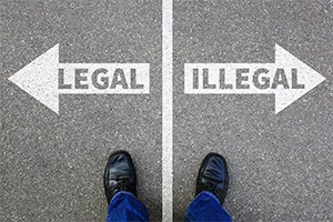 Looking down at a pair of feet straddling a white line on the pavement. One side has an arrow that says Legal and the other an arrow that says Illegal.