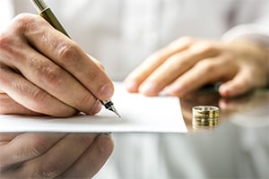 Man signing divorce papers with his wedding ring on the table next to him