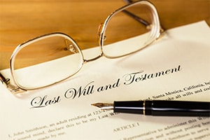 A copy of a last will and testament is laying on a table with a pen ready to sign it and a pair of glasses next to it