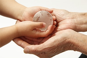 A elderly pair of hands cups a pair of child's hands. The child is holding a small glass globe in his hands.
