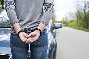 Recently arrested woman in handcuffs standing in front of her car on the side of the road