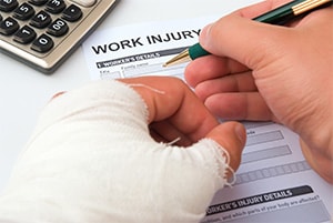 A close up of a man's hands filling out a work injury report. One hand is heavily bandaged.