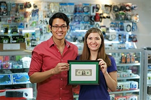 Small business law concept - Two small business owners stand in front of the counter at their shop holding their framed first dollar